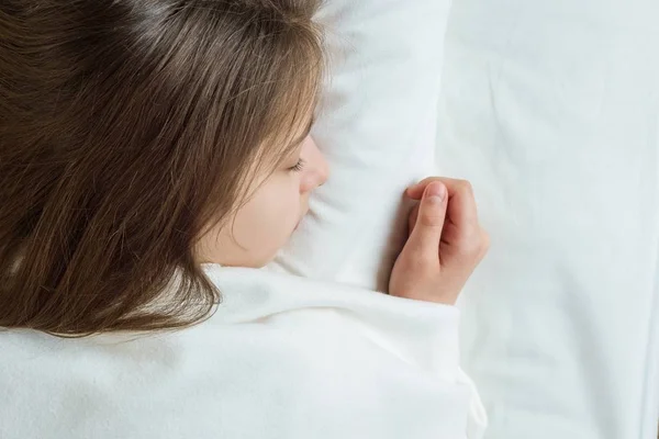 Menina criança com longos cabelos castanhos dormindo em um travesseiro na cama. Close up de meninas cabeça, na cama branca — Fotografia de Stock