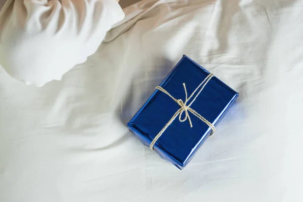 Gift surprise in bed, blue packed box on white bed — Stock Photo, Image