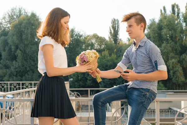 Jongen geeft meisje boeket van bloemen. Outdoor Portret van paar tieners, zonnige zomerdag — Stockfoto