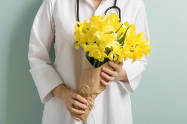 Buket sarı çiçek elinde bir kadın doktor, pastel yeşil nane duvar arka plan closeup. Dünya Sağlık günü, doktorlar gün