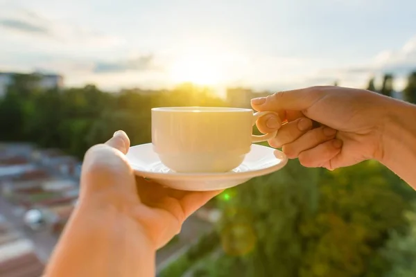 女性手捧着白杯和茶托。背景黄昏日落, 城市剪影 — 图库照片