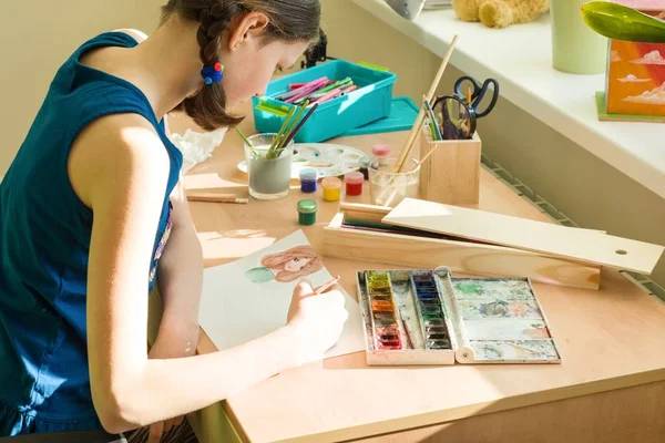 La muchacha adolescente en casa se ocupa de la obra, dibujando la acuarela a la mesa en la habitación. Creatividad infantil, recreación, desarrollo — Foto de Stock