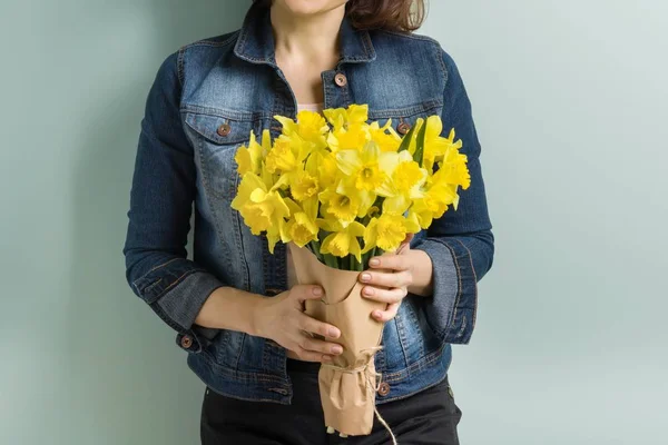 Bouquet of yellow flowers in hands of woman close-up, spring flowers daffodils, pastel green mint wall background. — Stock Photo, Image