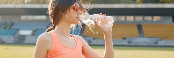 Młoda dziewczyna nastolatek pitnej wody z butelki po działa na stadionie, panoramiczny banner na słoneczny wiosenny wieczór — Zdjęcie stockowe