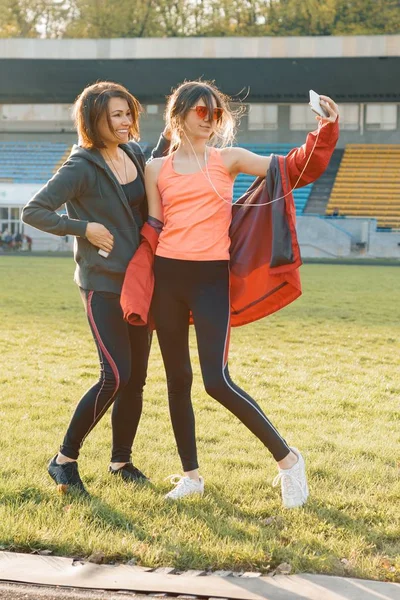 Healthy lifestyle, healthy family. Smiling fitness mother and teen daughter together posing at stadium after running on sunny spring evening