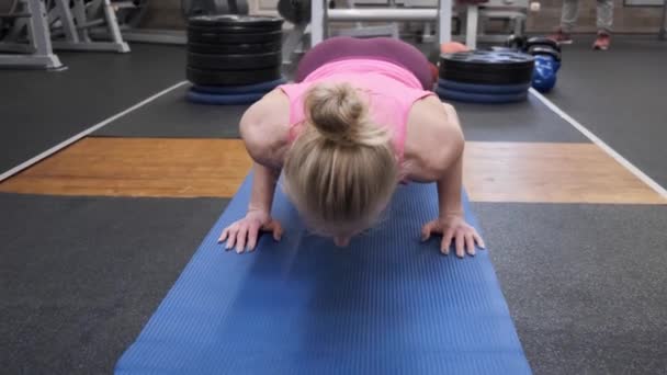 Hermosa atlética musculosa rubia haciendo ejercicio en el gimnasio, fitness femenina haciendo flexiones — Vídeo de stock