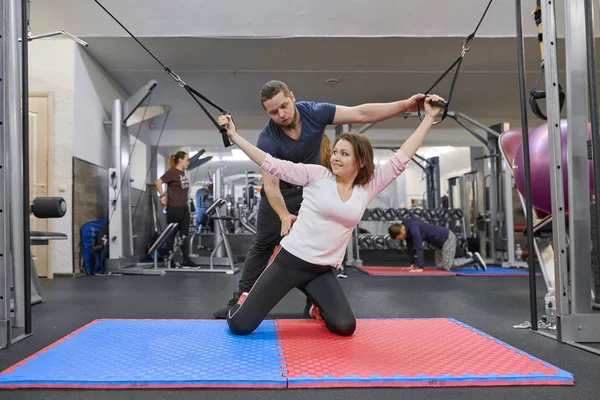 Kiev UA, 28-03-2019. Mujer madura haciendo ejercicio en simuladores de descompresión con rehabilitación de entrenador. Fisioterapeuta deportiva asistiendo a mujeres mayores. Tecnología Kinesio, kinesioterapia — Foto de Stock