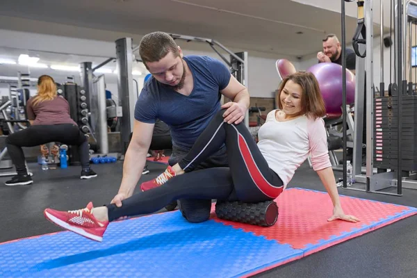 Kiev UA, 28-03-2019. Mujer madura haciendo ejercicios deportivos con entrenador personal en el gimnasio. Instructor masculino que ayuda a la mujer mayor — Foto de Stock