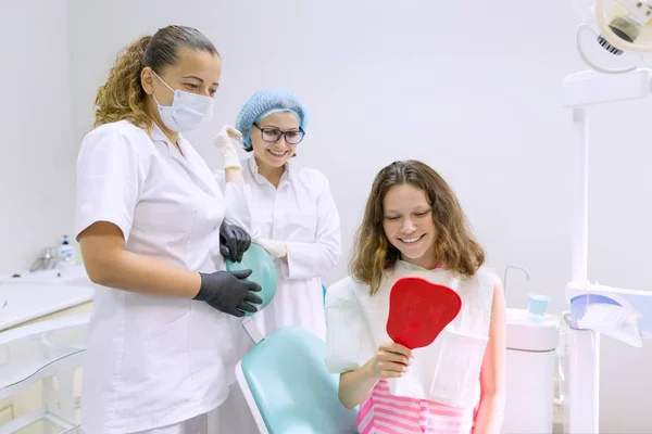 Niño feliz paciente mirando en el espejo a los dientes, sentado en la silla dental — Foto de Stock