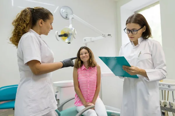 Nastoletnia dziewczyna siedzi w fotelu dentystycznym rozmawia z kobiecych dentystów. — Zdjęcie stockowe