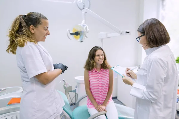 Дівчинка-підліток розмовляє з лікарями стоматологами, які сидять в стоматологічному кабінеті. Медицина, стоматологія та концепція охорони здоров'я — стокове фото