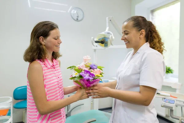 Meisje patiënt geeft een boeket bloemen aan een vrouwelijke arts in Dental Office. Nationale tandarts dag. — Stockfoto