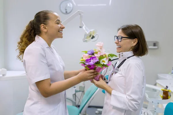 Zwei Zahnärztinnen mit einem Blumenstrauß in der Zahnarztpraxis. Nationaler Ärztetag. — Stockfoto