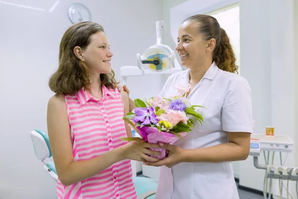Дівчина-пацієнт дарує букет квітів жінці-лікареві в стоматологічному кабінеті. Національний день стоматолога . — стокове фото