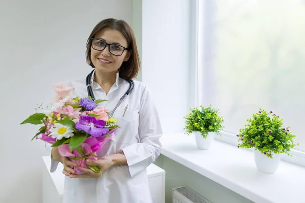 Woman doctor with bouquet of flowers, smiling near the window in the hospital. National Doctor's day.
