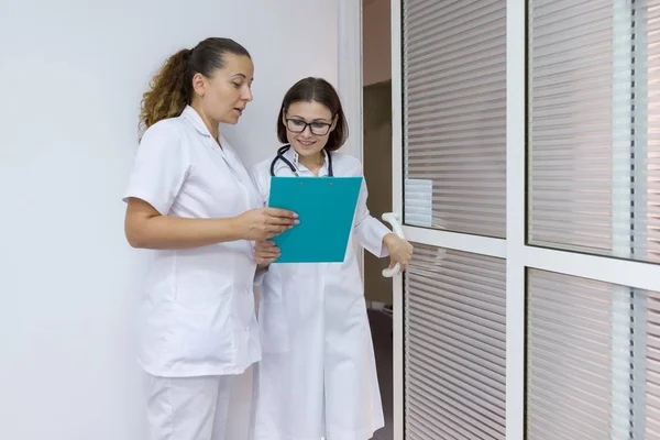 Duas mulheres médico e enfermeira conversando no hospital no fundo da porta — Fotografia de Stock