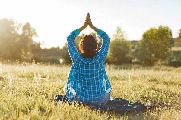 Vrouw mediteren, praktizerende yoga in de natuur, uitzicht vanaf de achterkant. Zonsondergang, rustieke landschappen, groene weide — Stockfoto