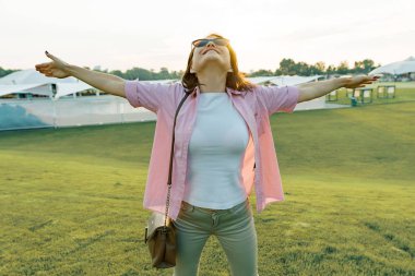 Orta yaşlı bir kadın bir tatil yaz eğlence bölgesinde, açık havada eller güneş ışığı Park yükselterek kadın sahiptir