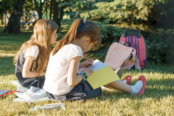 Две маленькие подружки школьницы учатся сидеть на лугу в парке. Дети с рюкзаками, книгами, блокнотами. Вид сзади — стоковое фото