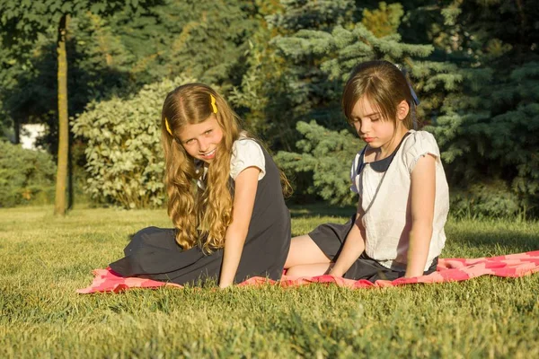 Portrait of two girls friends 7, 8 years old sitting on the grass in the park, golden hour