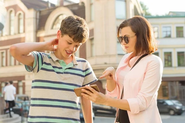 Padres y adolescentes, relación. Madre e hijo adolescente están mirando el teléfono móvil, fondo de la calle de la ciudad —  Fotos de Stock