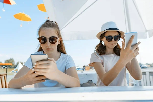 Jovens meninas adolescentes com telefones celulares. Sente-se em um café de rua, dia ensolarado de verão na área de recreação e entretenimento — Fotografia de Stock