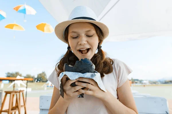 Teen girl with an appetite eats black fast food burger. Summer street cafe, recreation area, city park background — Stock Photo, Image