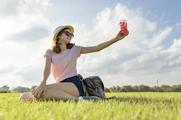 Fiatal lány napszemüveg és kalap nyári bogyó ital italok, jég ül a zöld fű, másolja a hely, arany óra — Stock Fotó