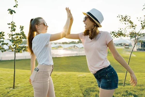 La amistad de dos chicas adolescentes, mejores novias se divierten en la naturaleza, en el césped verde del parque de recreo y entretenimiento. Abrace el saludo y la despedida . — Foto de Stock