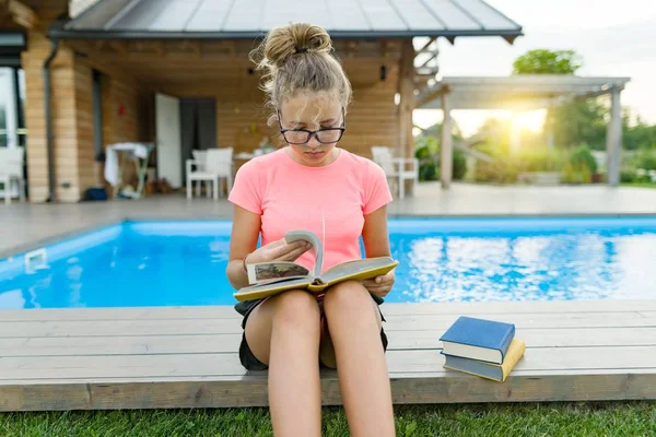 Mladá dívka v brýlích u bazénu s hromadu knih, čtení knihy. Vzdělání, léto, znalosti — Stock fotografie