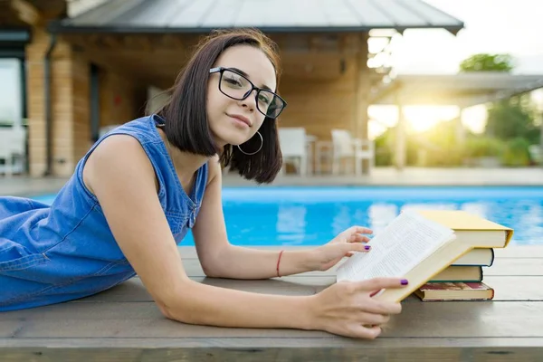 可爱的学生女孩阅读躺在游泳池附近的书。教育、暑期、知识 — 图库照片