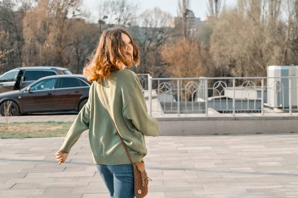 Прогулка молодая улыбающаяся девочка подросток, глядя в камеру через спину с каштановыми рыжими волосами в зеленом свитере, солнечный весенний день фон, копировальное пространство — стоковое фото