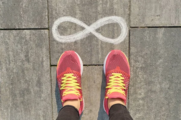 Signo infinito en la acera gris con piernas de mujer en zapatillas de deporte, vista superior — Foto de Stock