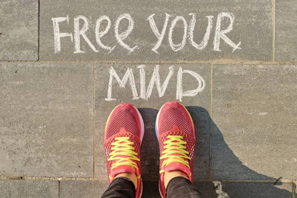 Free your mind text on gray sidewalk with woman legs in sneakers, top view