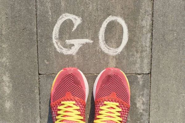 Palabra ir escrito en la acera gris con las piernas de las mujeres en zapatillas de deporte, vista superior — Foto de Stock