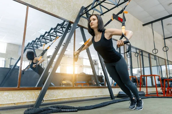Giovane bella donna sportiva che si esercita sul sistema di cinghie di fitness in palestra. Fitness, sport, allenamento e stile di vita sano . — Foto Stock