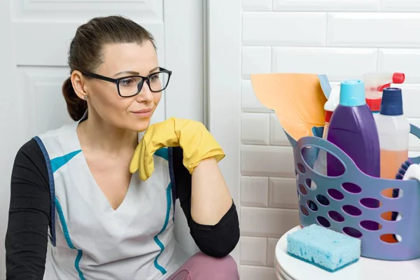 Donna adulta che fa pulizia con detergenti. Donna in occhiali, uniforme professionale in bagno, toilette in camera — Foto Stock