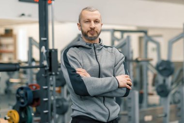 Spor salonunda katlanmış eller ile sportif adam portresi, yakışıklı sakallı antrenör kamera bakıyor