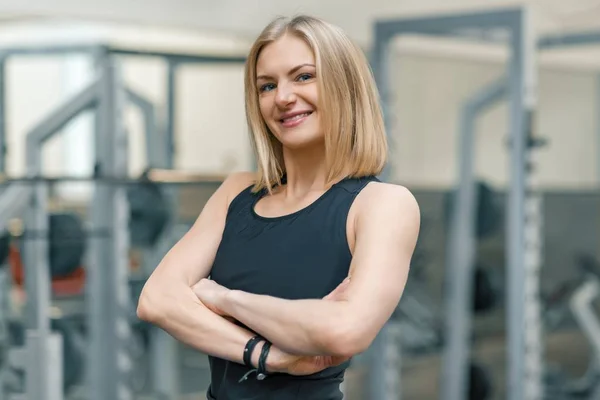 Ritratto di donna fitness bionda adulta personal trainer con mani incrociate in palestra, bella donna sorridente che guarda in macchina fotografica — Foto Stock