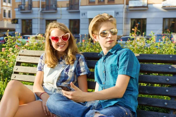 Друзі-підлітки дівчинка і хлопчик сидять на лавці в місті, розмовляють. Концепція дружби і людей — стокове фото