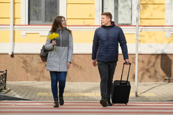 Retrato ao ar livre de jovem casal andando com mala na rua da cidade, jovem feliz e mulher viajam na primavera, pessoas na travessia de zebra, fundo urbano — Fotografia de Stock