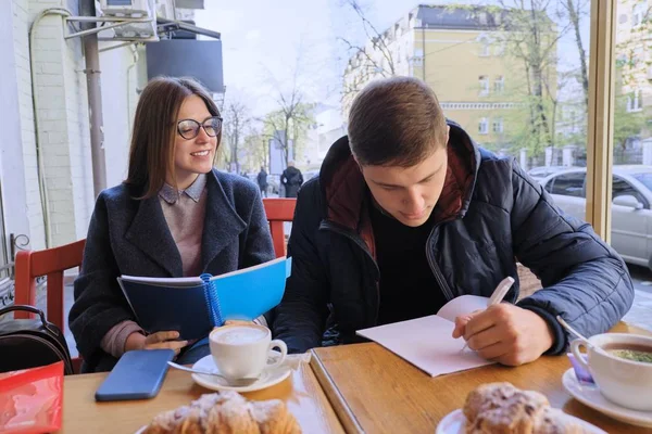 Pareja joven de estudiantes estudian en la cafetería al aire libre, beber té de café, comer croissants, fondo es la calle de la ciudad de primavera — Foto de Stock