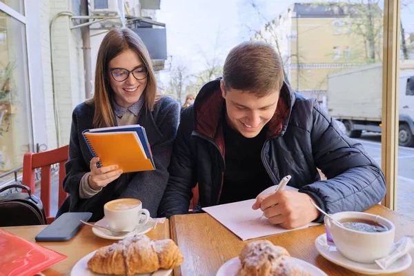 Pareja joven de estudiantes estudian en la cafetería al aire libre, beber té de café, comer croissants, fondo es la calle de la ciudad de primavera — Foto de Stock