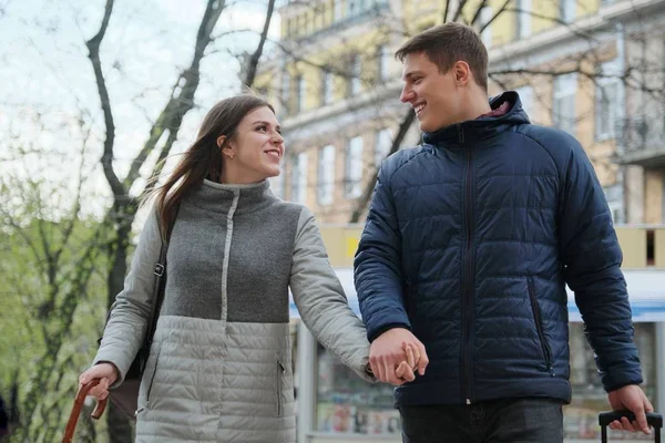 Outdoor portrait of young couple walking with suitcase on city street, happy young man and woman travel in spring, urban background — стоковое фото