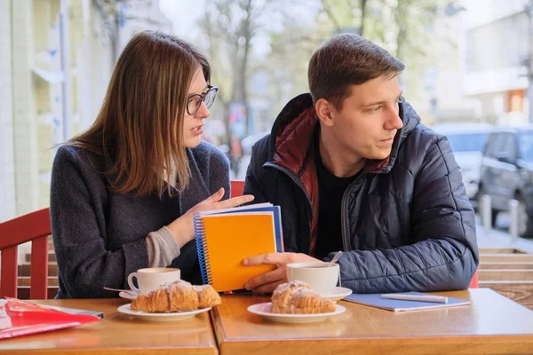 Pareja joven de estudiantes estudian en la cafetería al aire libre, beber té de café, comer croissants, fondo es la calle de la ciudad de primavera — Foto de Stock