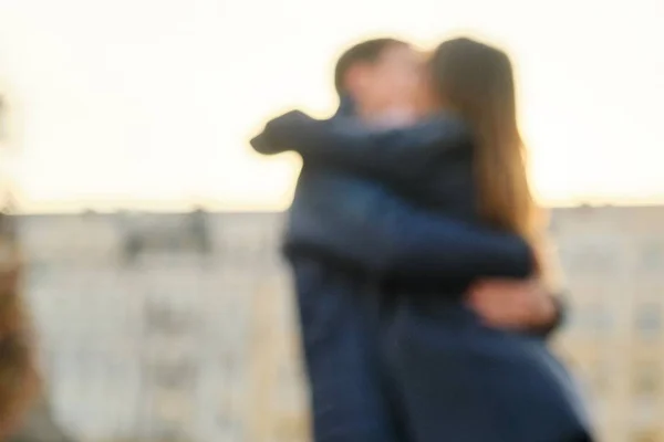 Ung man och kvinna kramar kyssar, par suddig och mjuk fokus, bakgrund stad, gyllene timme — Stockfoto