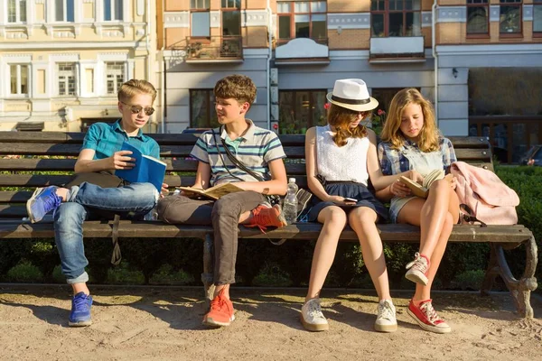 Feliz 4 amigos adolescentes ou estudantes do ensino médio estão se divertindo, conversando, lendo telefone, livro. Conceito de amizade e pessoas, cidade rua fundo — Fotografia de Stock