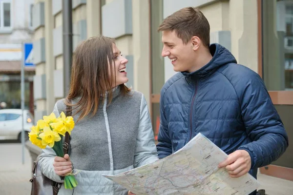 Un par de turistas cariñosos. Joven sonriente hombre y mujer leyendo mapa, chica con ramo, fondo de la ciudad de primavera . —  Fotos de Stock