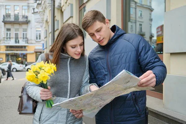 Un par de turistas cariñosos. Joven sonriente hombre y mujer leyendo mapa, chica con ramo, fondo de la ciudad de primavera . — Foto de Stock