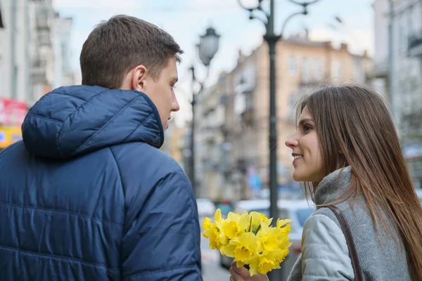 Casal apaixonado na cidade. Jovem homem e mulher feliz na cidade da primavera falando, andando, com buquê de flores amarelas narcisos — Fotografia de Stock